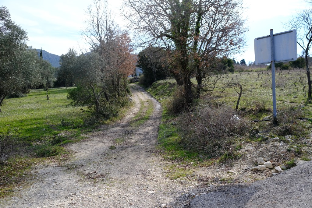A gravel pathway winding through a green landscape with trees and a blank signpost on the right.